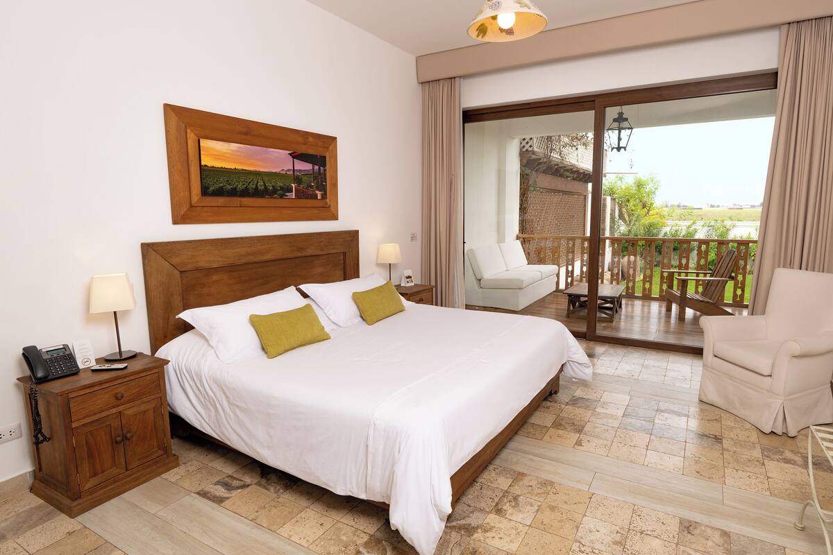 Une chambre d’hôtel comprenant un lit, des tables de chevet, une chaise, un balcon avec vue et une tête de lit en bois.