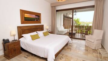 Habitación de hotel con cama, mesitas de noche, una silla, balcón con vistas y cabecero de madera.