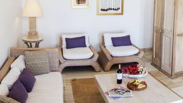 A cozy room with a sofa, two wicker chairs, a small table with a bottle and flowers, and a cabinet.