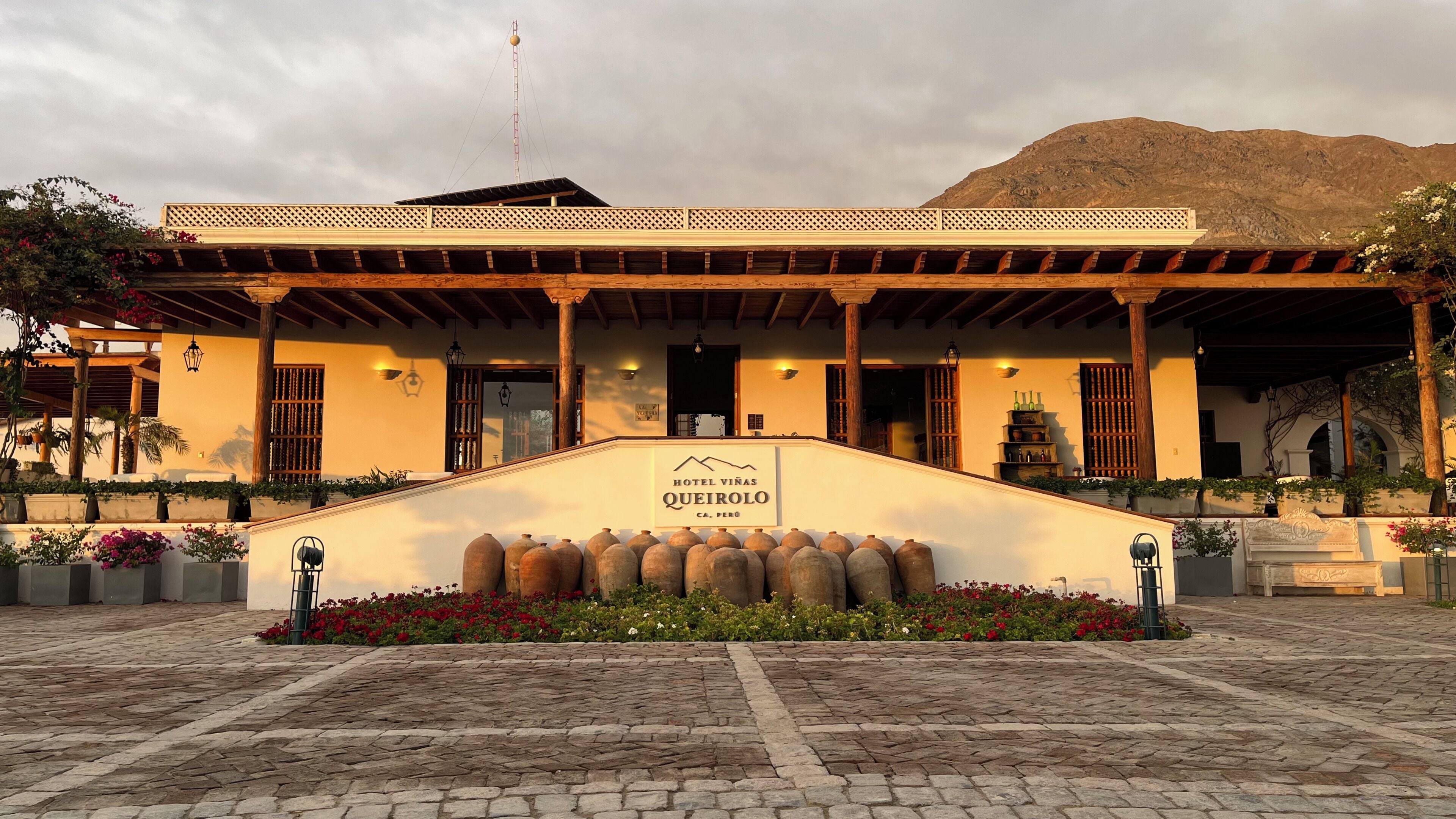 A hotel entrance with a sign reading 'Hotel Viñas Queirol,' a covered patio area, and a mountainous backdrop.