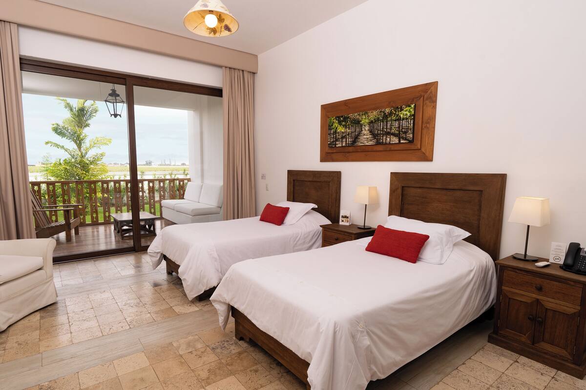 Une chambre d’hôtel avec deux lits, un balcon, un canapé et un tableau au mur.