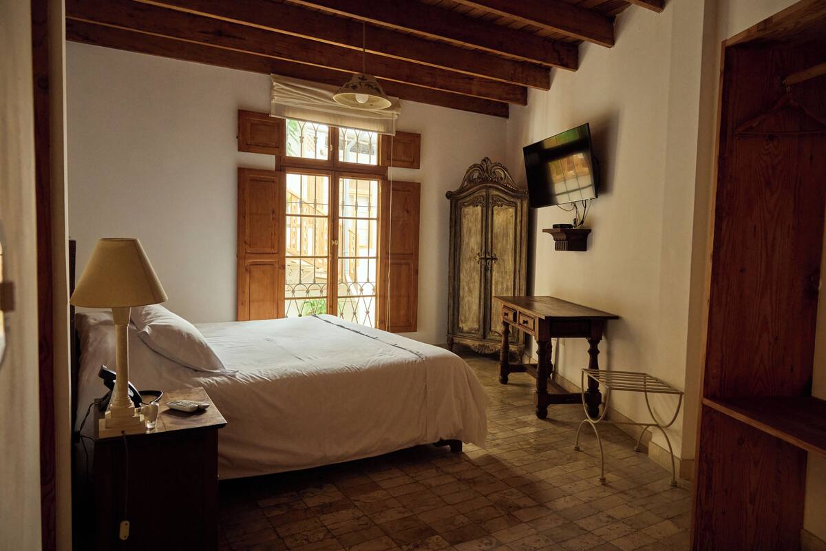 Une chambre à coucher comprenant un lit, une table de chevet, une lampe, une armoire en bois, un miroir et une porte en bois.