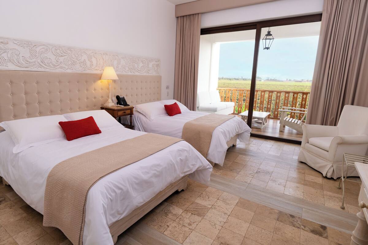 Une chambre d’hôtel avec deux lits, une table de chevet avec une lampe, une chaise et une vue sur l’extérieur.