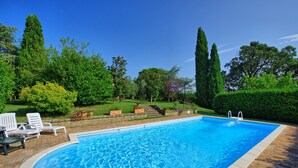 Una piscina rectangular con superficie de agua azul cristalina, rodeada por una terraza de madera y sillas reclinables blancas.