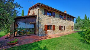 Una casa de piedra con un amplio ventanal y ventanas, rodeada de un césped cuidado y árboles.