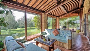 Un amplio patio con mobiliario de mimbre, una mesa de centro con adornos y ventanas grandes que dan a un jardín exuberante.