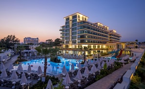 Un hôtel à plusieurs étages doté d’un espace piscine, comprenant des chaises longues et des parasols.