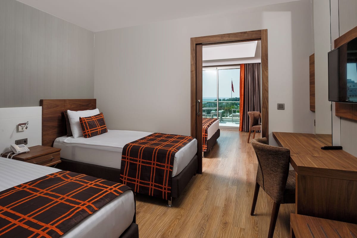 A hotel room with two beds, a desk, a chair, a TV, and a balcony with a view.