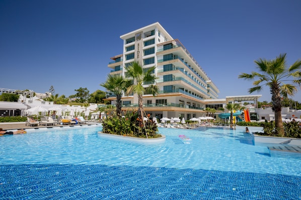 Un hôtel moderne doté d’une grande piscine, de palmiers et surplombant un ciel d’un bleu éclatant.
