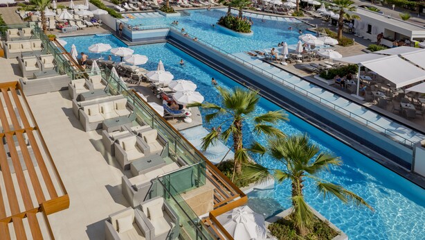 A large outdoor swimming pool with multiple lanes, surrounded by lounge chairs and umbrellas, and palm trees. - Side Sunport Hotel & Spa - All Inclusive (Manavgat)