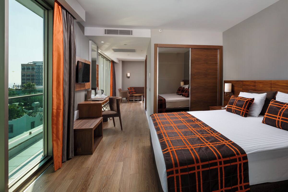 A hotel room with a large bed, a desk, a chair, a TV, and a view of the city.