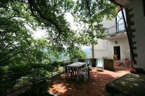 An outdoor patio with a table and chairs, surrounded by lush greenery and a view of a building.