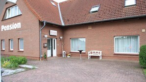 Ein Backsteinhaus mit einem Schild, auf dem "Pension" steht, und einer kleinen Außenbestuhlung mit einer Bank und einem Tisch.