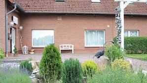 Ein Ziegelhaus mit zwei großen Fenstern, einer weißen Bank und einem Garten mit verschiedenen Pflanzen.