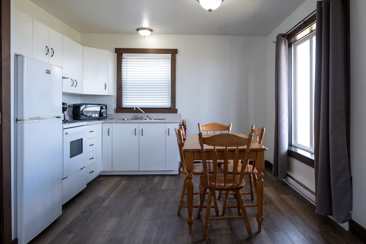 Cocina compacta con armarios blancos, microondas, fregadero y mesa de comedor con sillas.