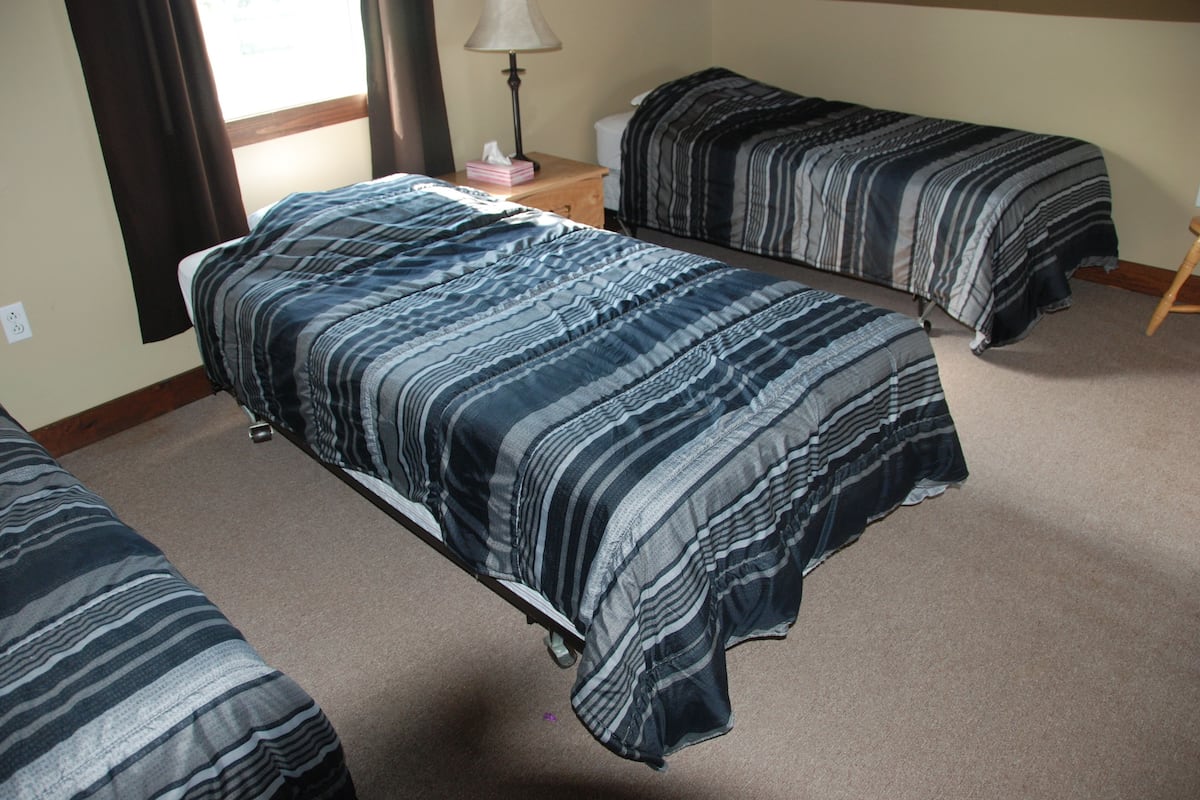 Un dormitorio con dos camas individuales, una mesita de noche con lámpara y una ventana con cortinas.