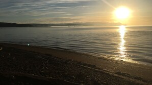 A beach with a calm sea and a setting sun.
