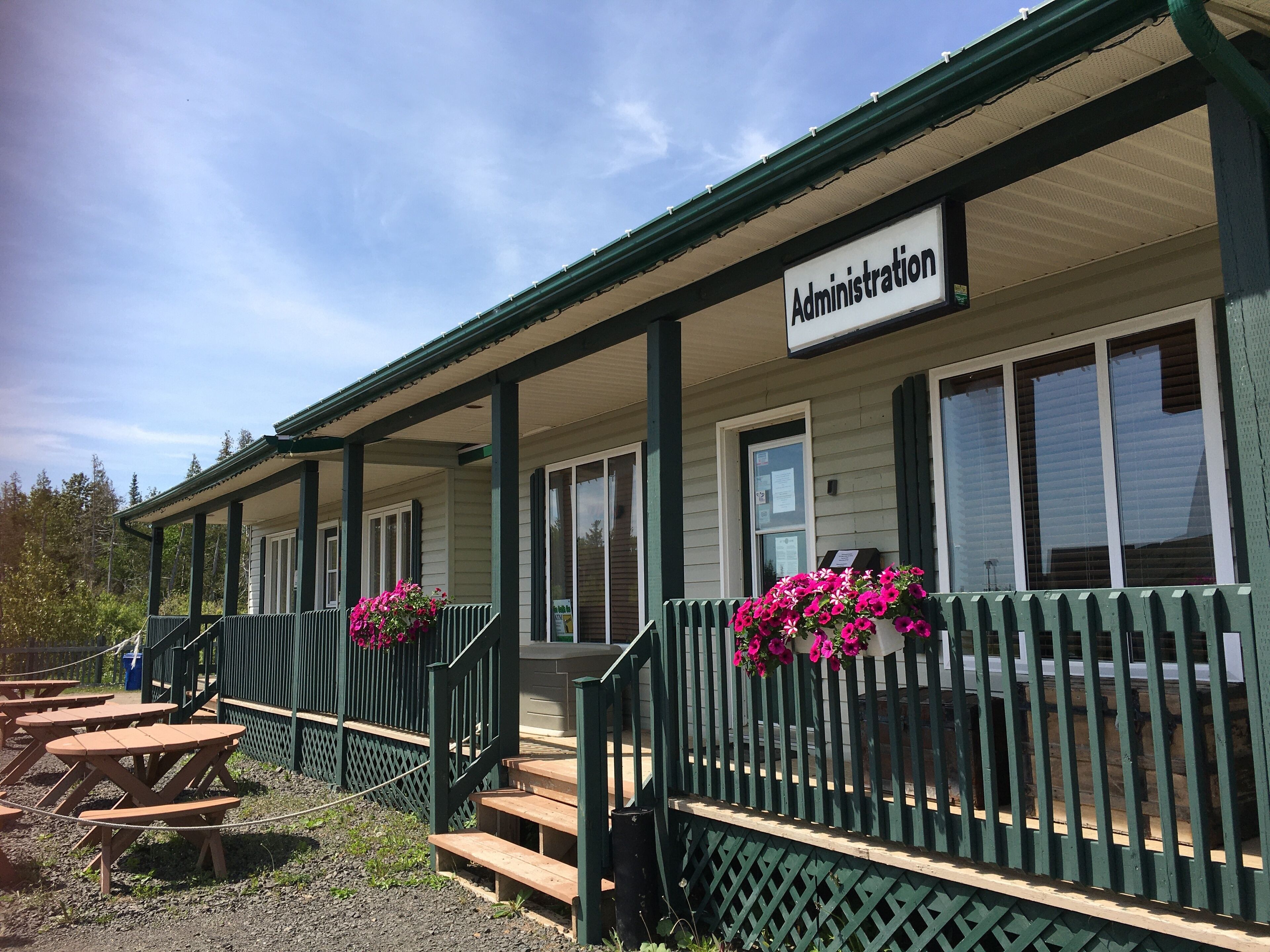 A building with a sign reading "Administration" and a covered porch with wooden benches and flower pots.
