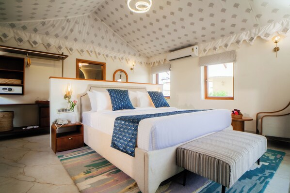 A hotel room with a bed, bedside table, lamp, and a view of the outdoors.