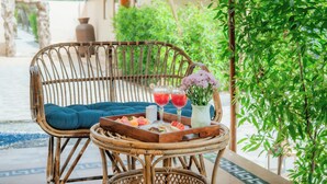 A wicker chair with a blue cushion, a tray with fruit and drinks, and a vase with flowers.