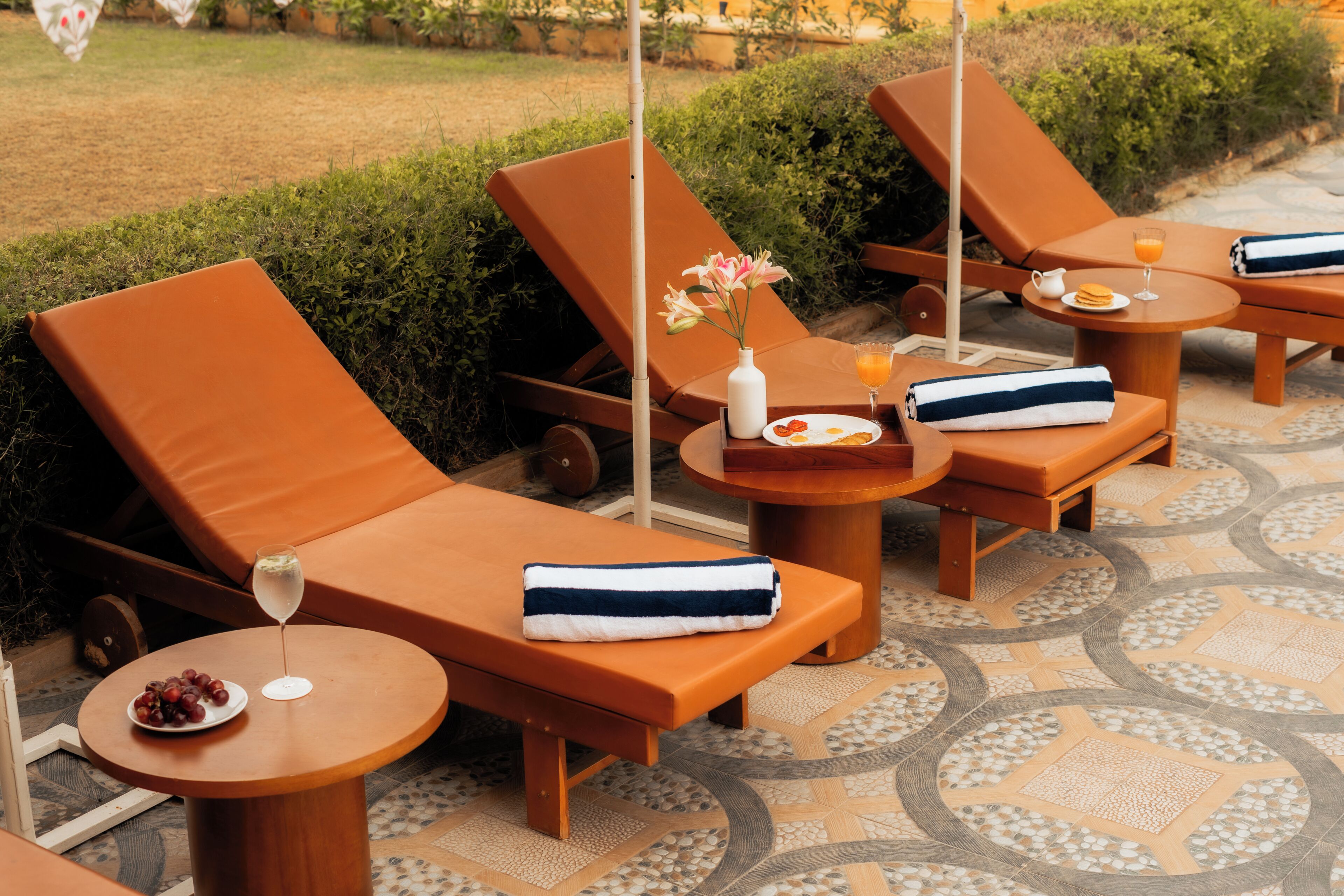 A set of sun loungers with towels and a glass of orange juice on a tiled patio.