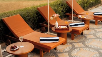A set of sun loungers with towels and a glass of orange juice on a tiled patio.