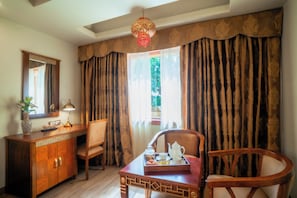 A hotel room with a wooden desk, a chair, a dresser, a mirror, and a window with curtains.