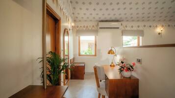 A room with a wooden desk, a chair, a potted plant, and a window with a view of greenery.
