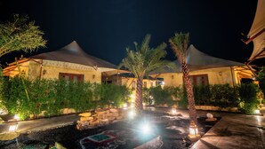 A courtyard with tents, palm trees, and a decorative water feature at night.