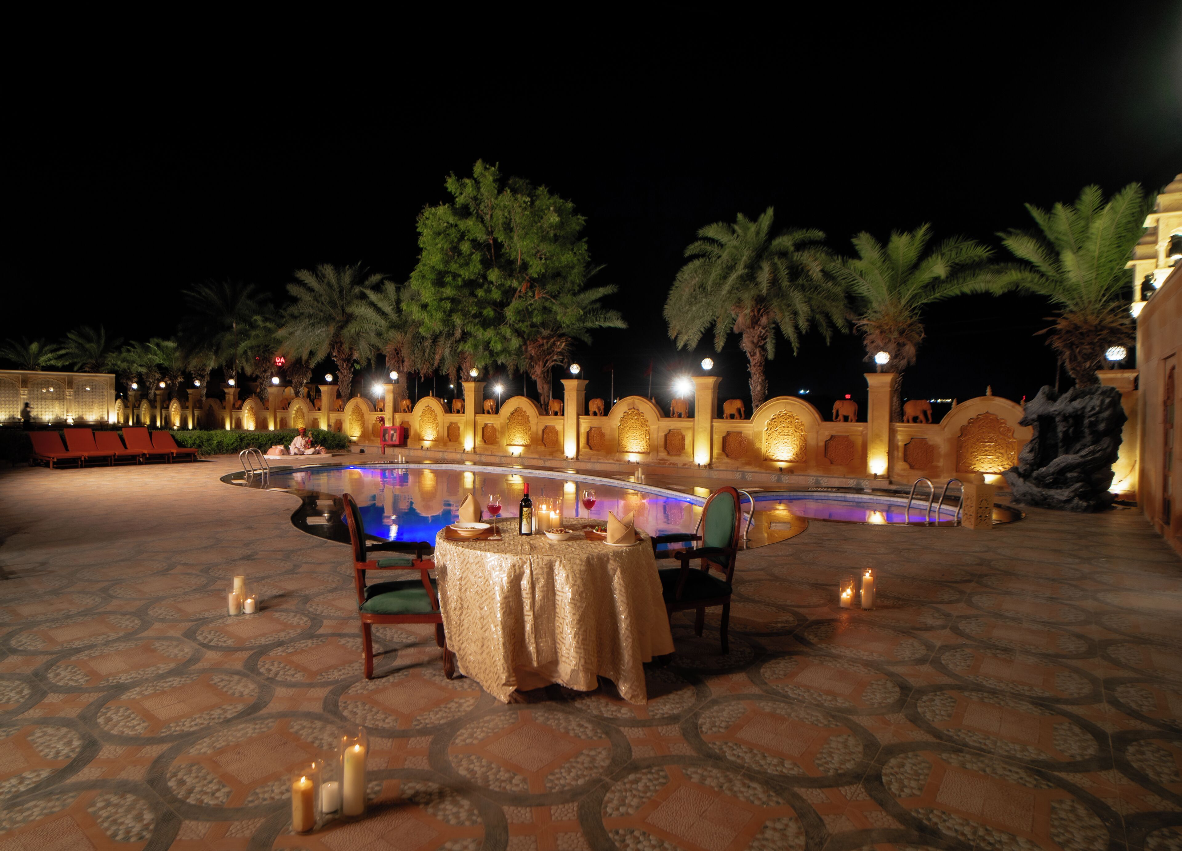 An outdoor dining area with a pool, palm trees, and a decorative wall with animal statues.