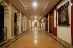A long, narrow hallway with a polished floor, doors on both sides, and a mirror on the right wall.