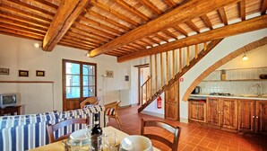 Un comedor con una mesa dispuesta para cuatro personas, una escalera de madera y una cocina con armarios de madera.