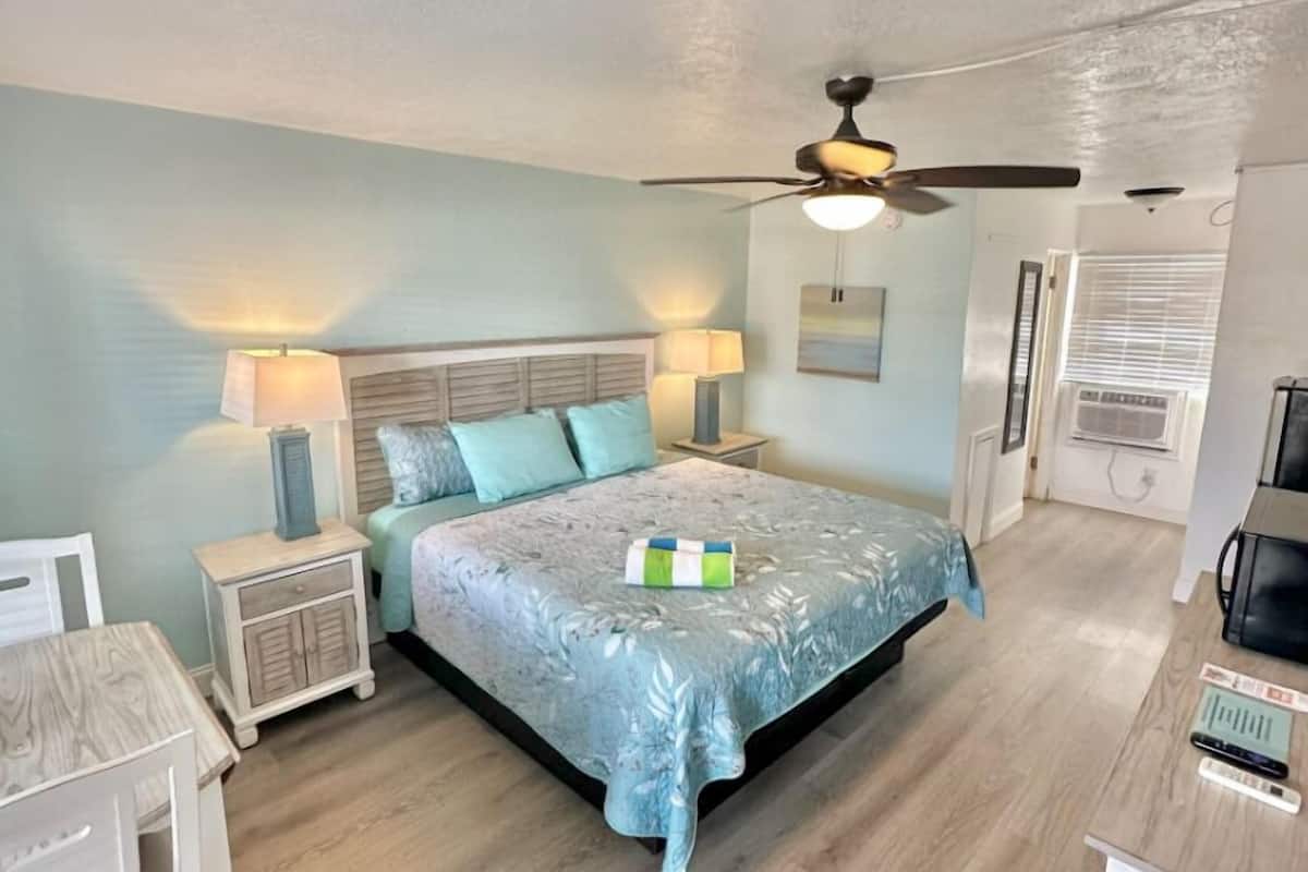 A bedroom with a bed, nightstands, a desk, a ceiling fan, and a window with blinds.