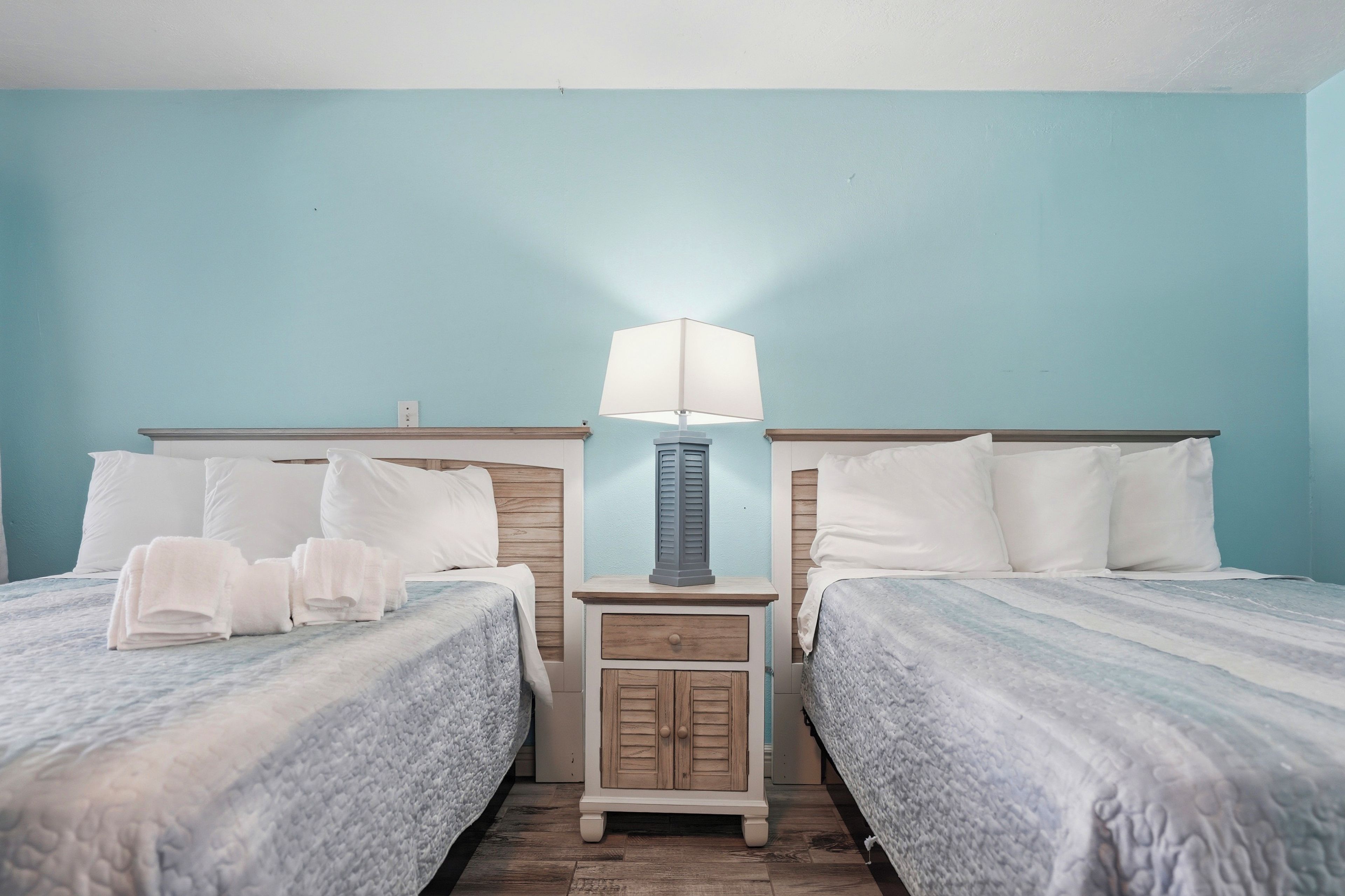 A hotel room with two beds, a nightstand with a lamp, and a small cabinet.