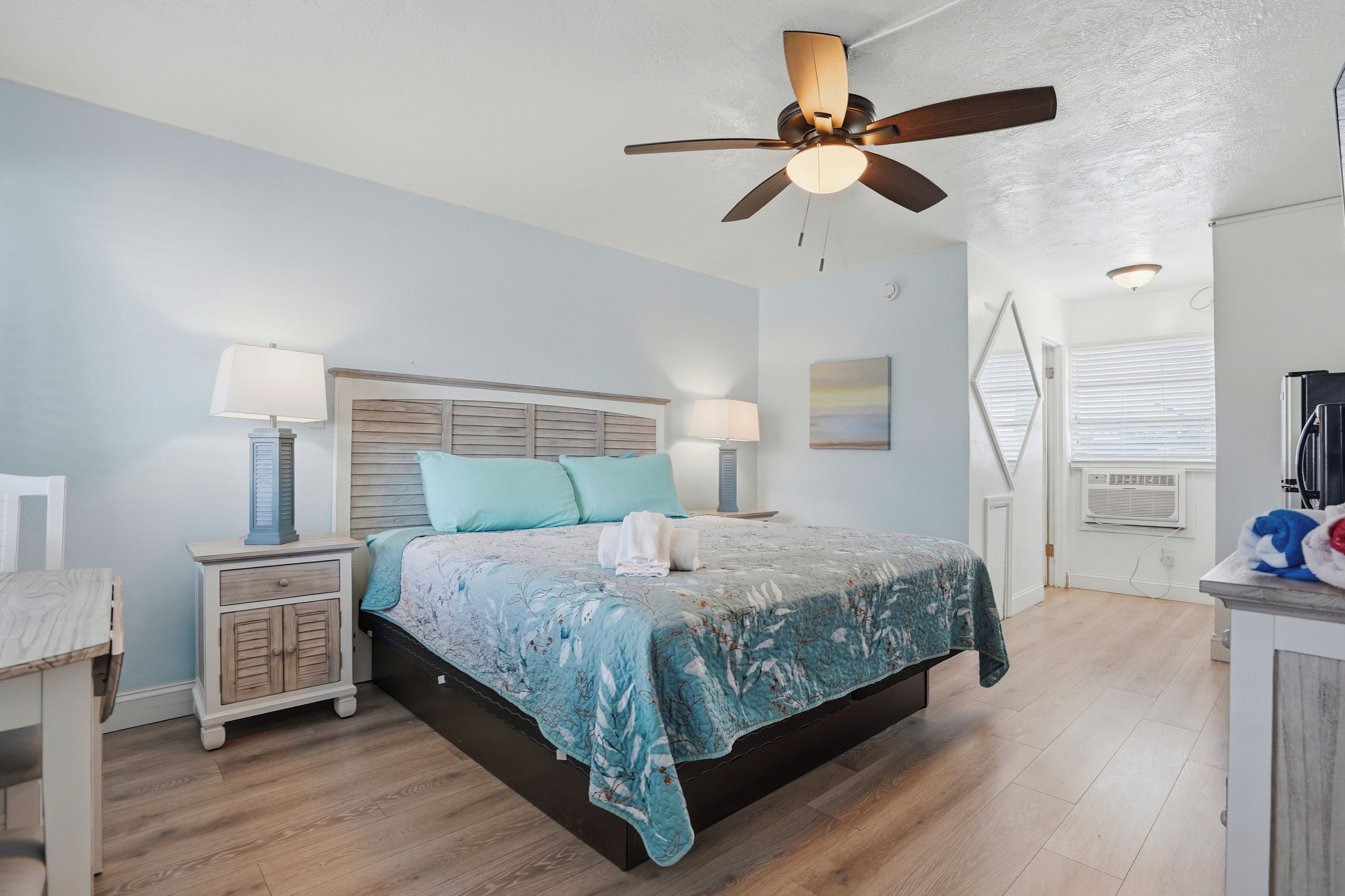 A bedroom with a bed, two bedside tables, a ceiling fan, and a window with blinds.