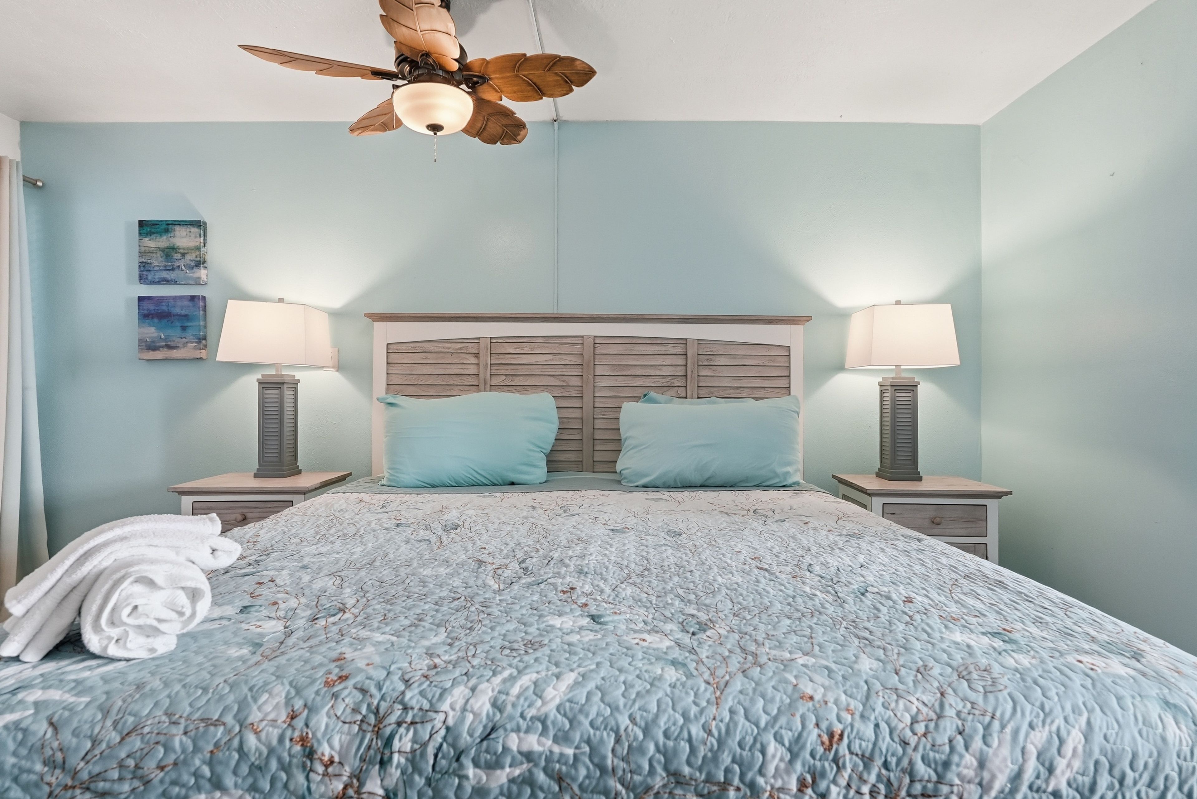 A bedroom with a bed, two bedside lamps, a ceiling fan, and a headboard.