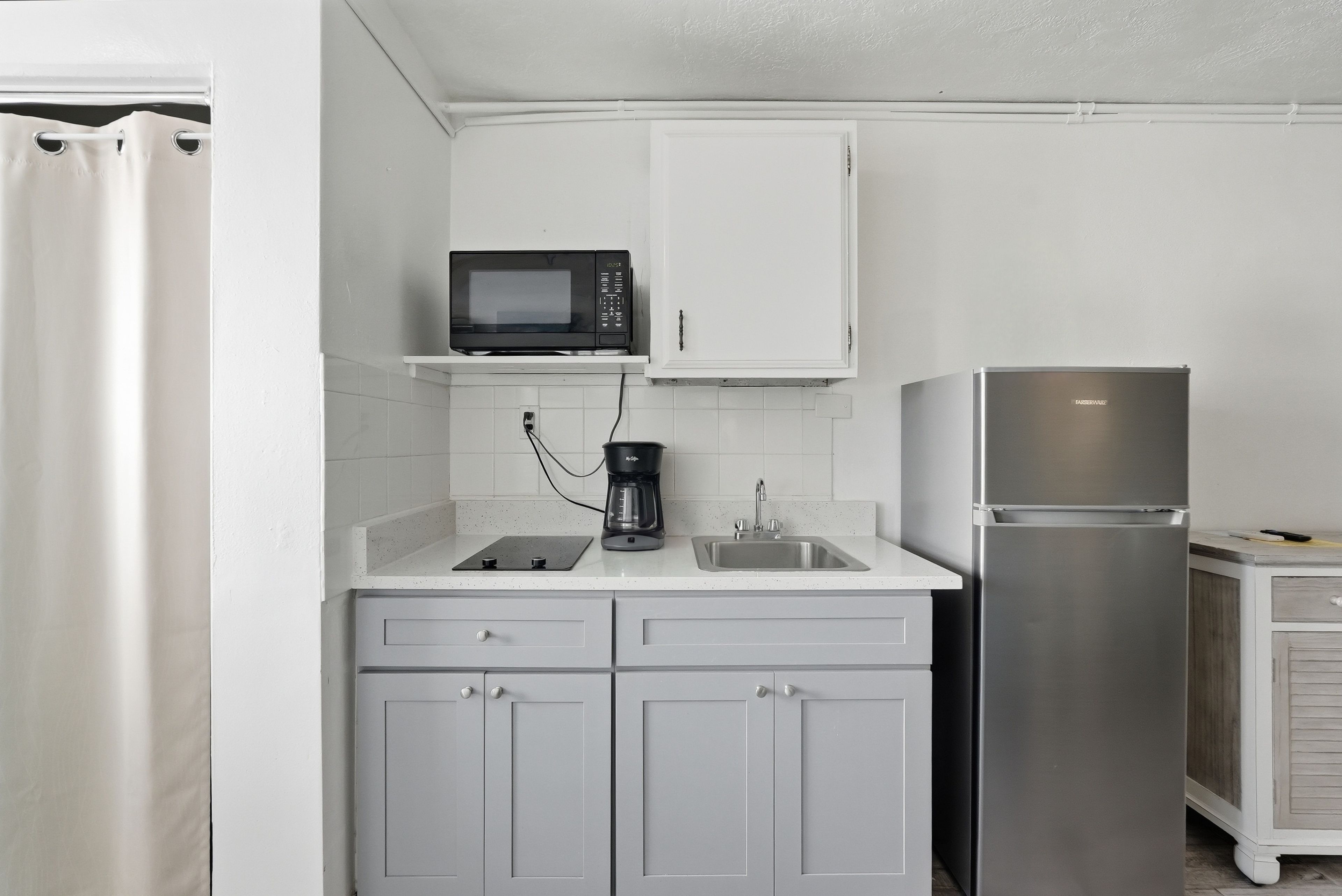 A compact kitchenette with a microwave, coffee maker, sink, and a stainless steel refrigerator.