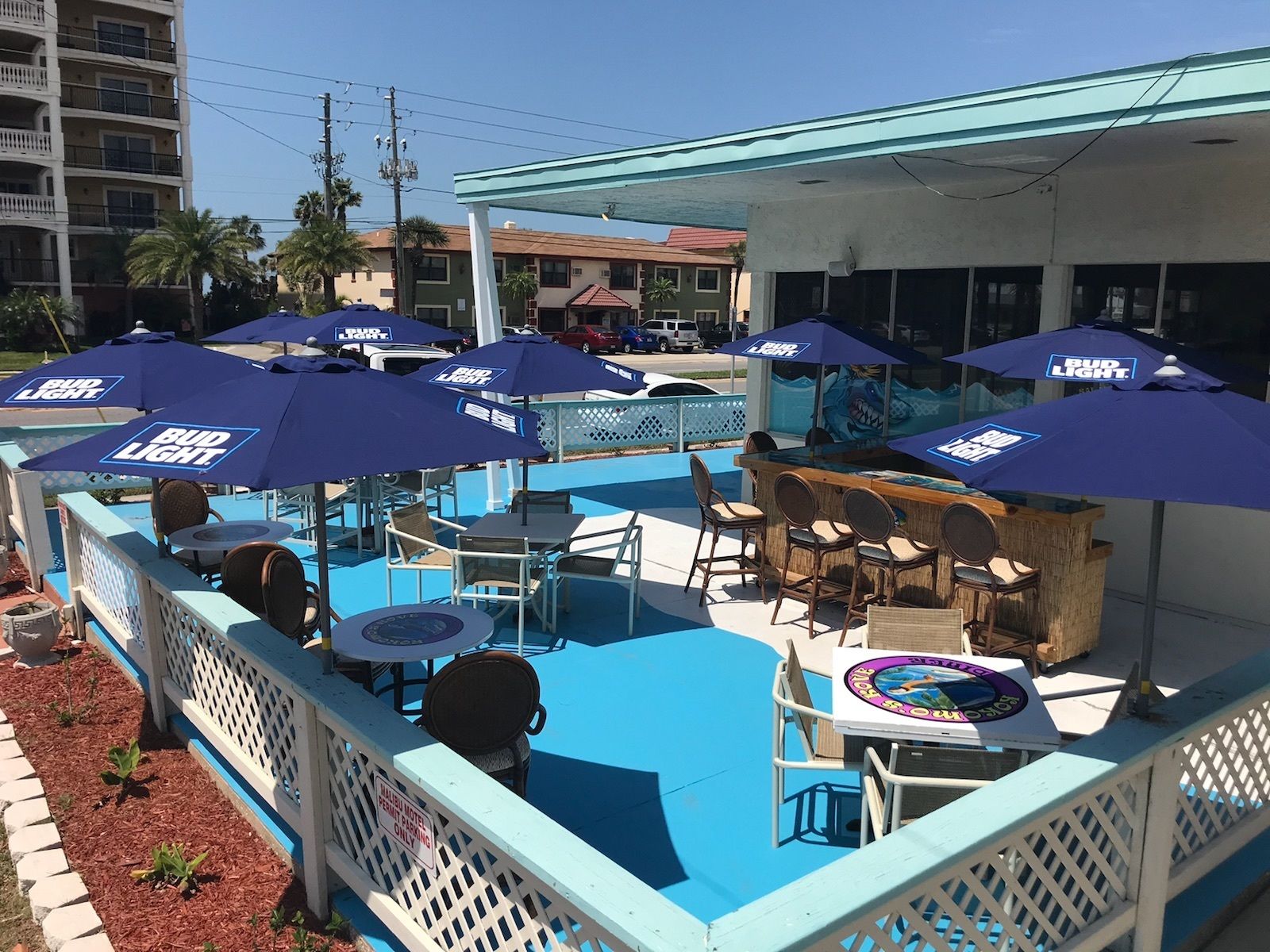 Un área de piscina al aire libre con varias sombrillas de Bud Light, sillas de descanso y un bar.