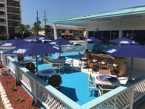 An outdoor pool area with multiple Bud Light umbrellas, lounge chairs, and a bar area. - Malibu Resort Motel (North Redington Beach)