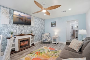A living room with a fireplace, a ceiling fan, a television, and a sofa. - Malibu Resort Motel (North Redington Beach)