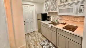 Una cocina con microondas, lavamanos y armarios.