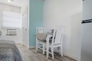A small room with a bed, a table with chairs, a window with blinds, and a door.