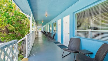 A covered corridor with rows of wicker chairs and a row of doors.