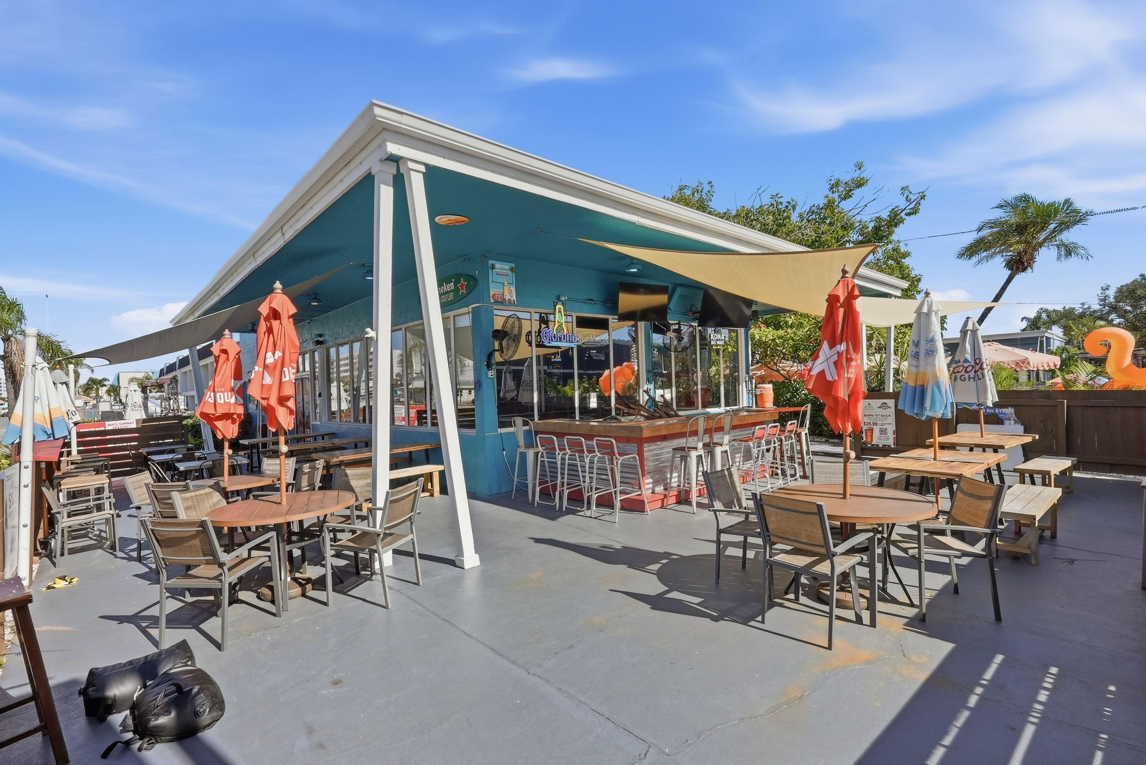 An outdoor café with tables and chairs, a bar area, and umbrellas.