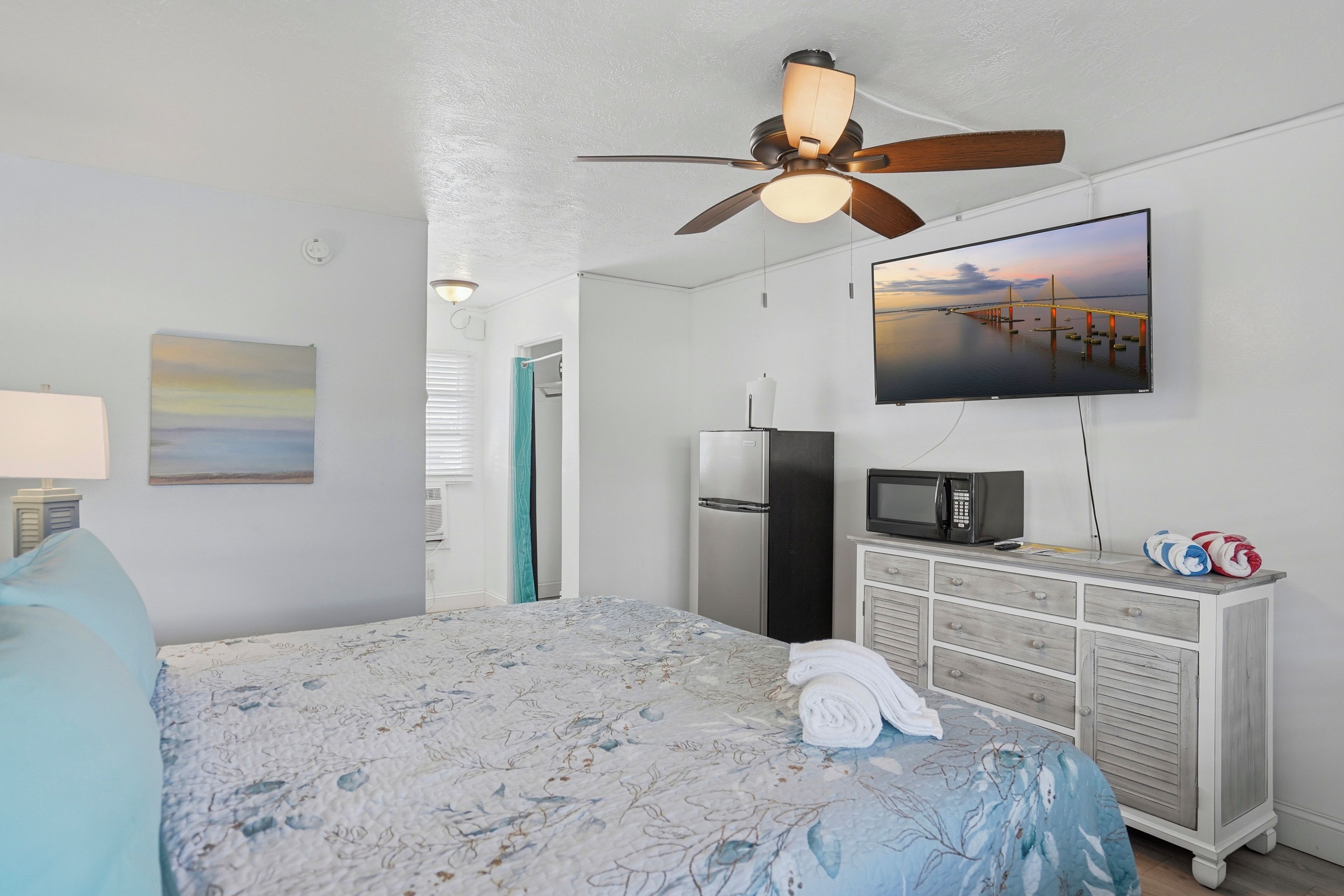 Une chambre d’hôtel équipée d’un lit, d’un ventilateur de plafond, d’un téléviseur à écran plat, d’un réfrigérateur, d’un four à micro-ondes et d’une commode.