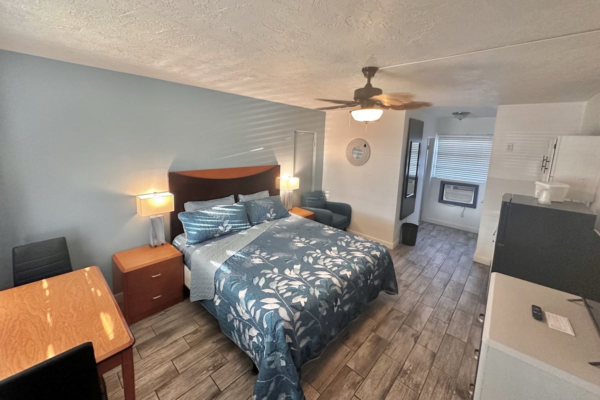 A bedroom with a bed, bedside tables, a ceiling fan, a desk, and a chair.