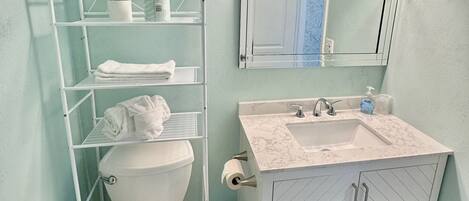 A bathroom with a white toilet, a sink with a marble countertop, a mirror above the sink, and a towel rack with folded towels.