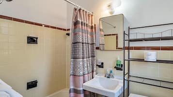 A bathroom with a shower curtain, a sink, a mirror, and a shelf with toiletries.