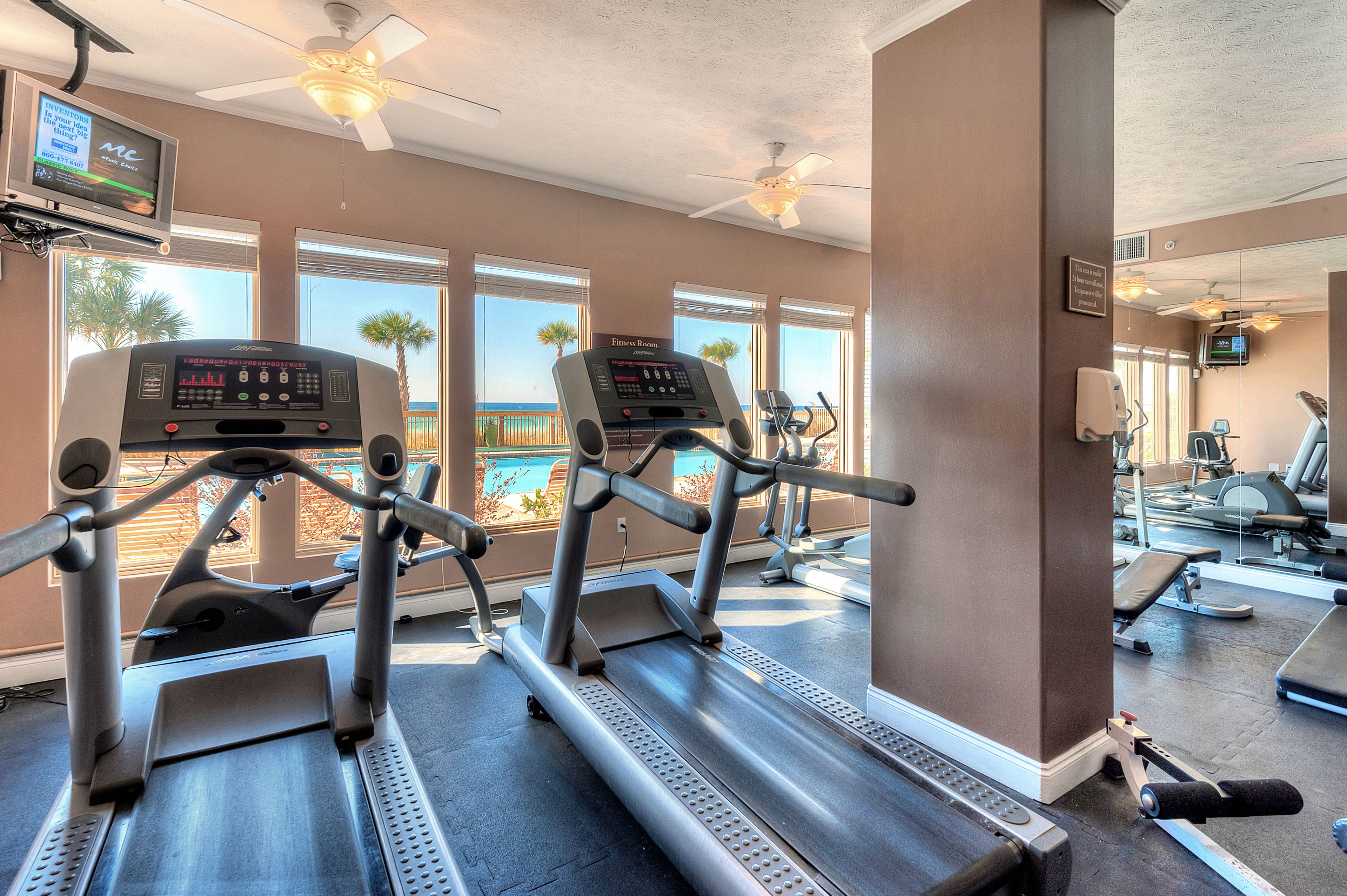 A gym with treadmills, a TV, and a view of the beach.
