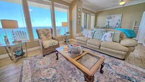 A living room with a view of the sea, a sofa, a chair, and a coffee table. - Gulf Crest Condominiums (Panama City Beach)